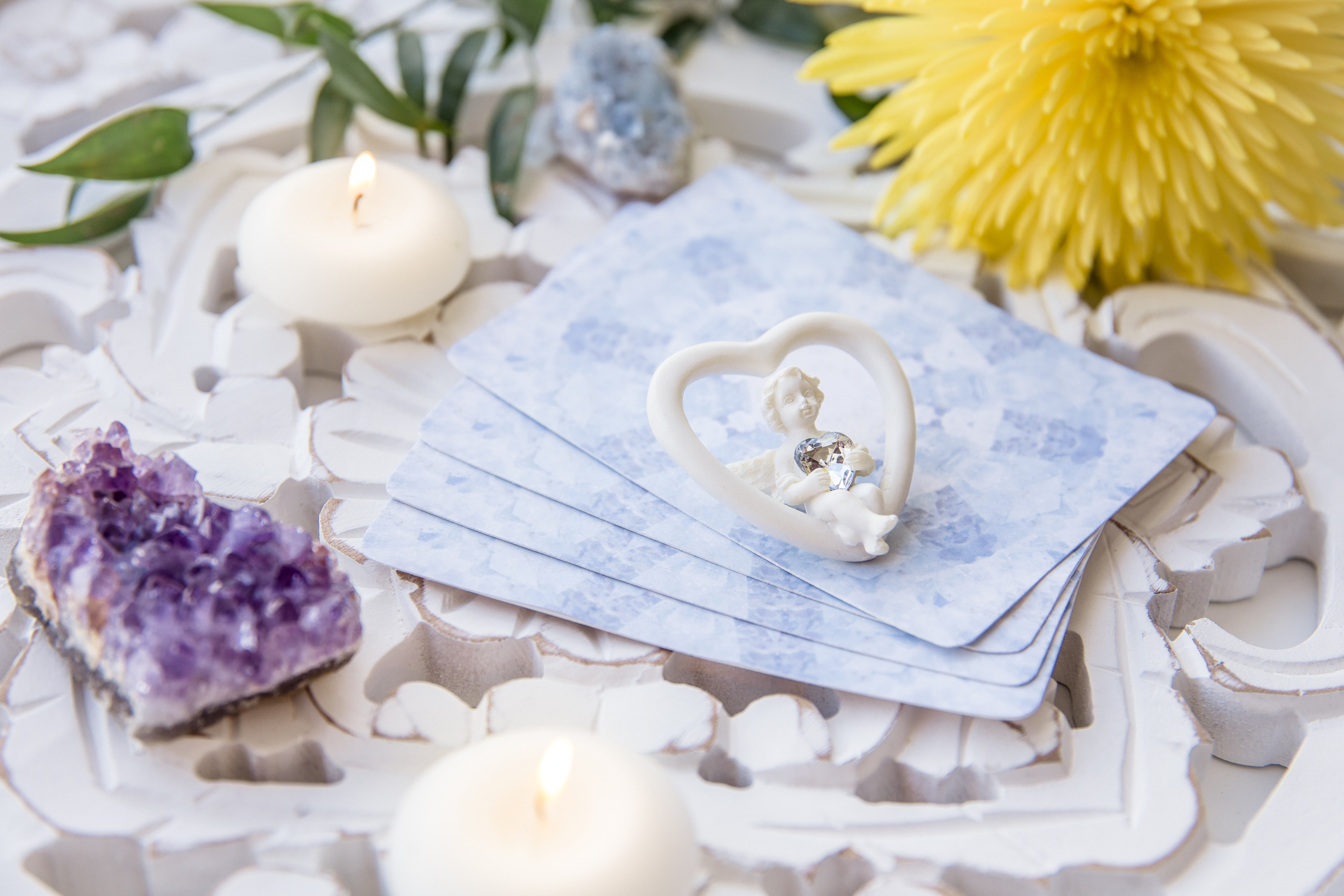 Deck with divination homemade Angel cards on bright white table, surrounded with semi precious stones crystals and candles. Selective focus on cute angel figurine.